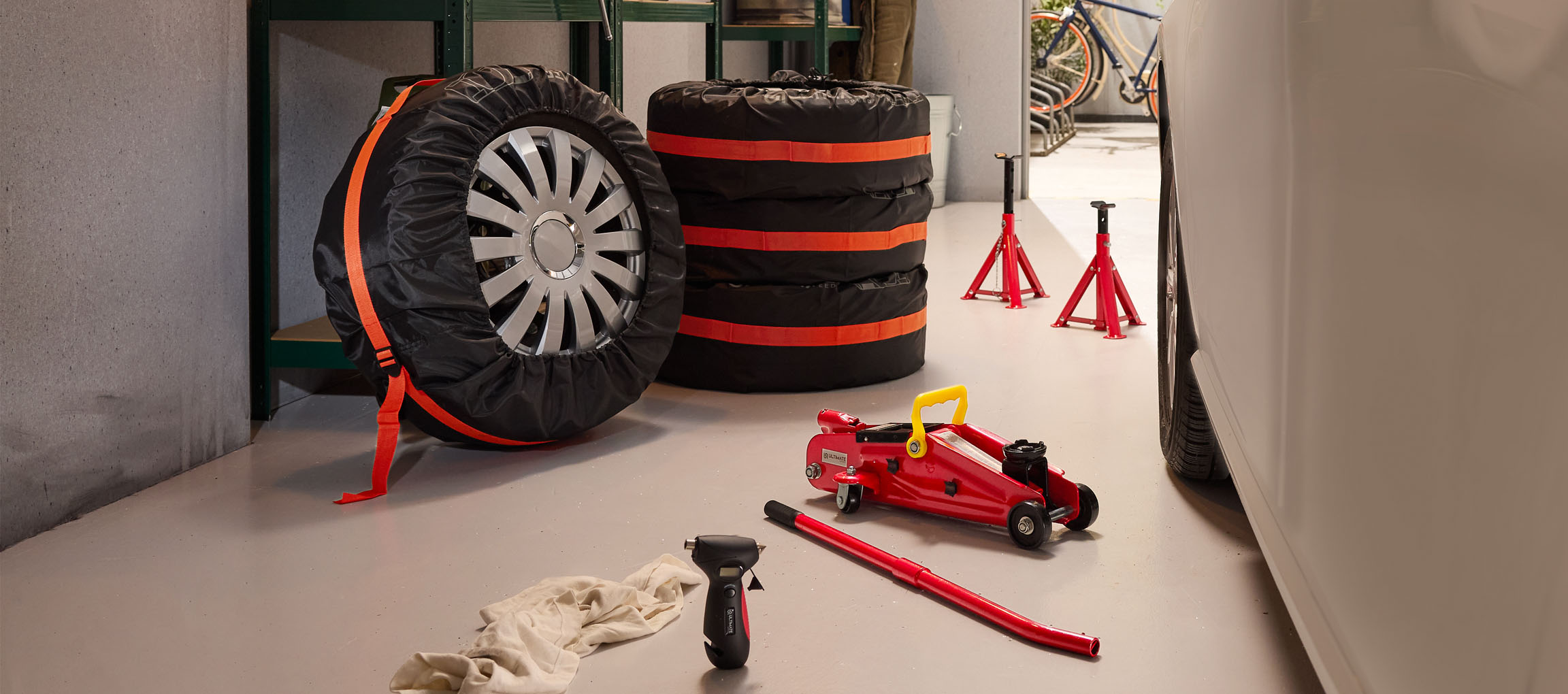 Automašīnas riepas ar pārvalkiem, domkrats un statīvi garāžā.