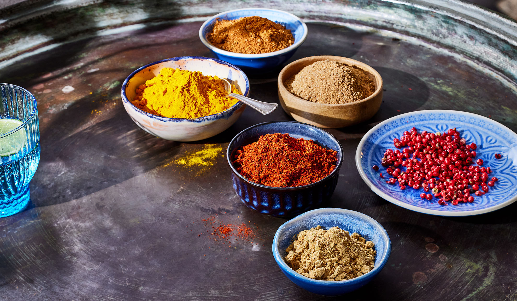 Dažādas garšvielas bļodiņās: kurkuma, paprika, pipari un citas uz metāla paplātes.