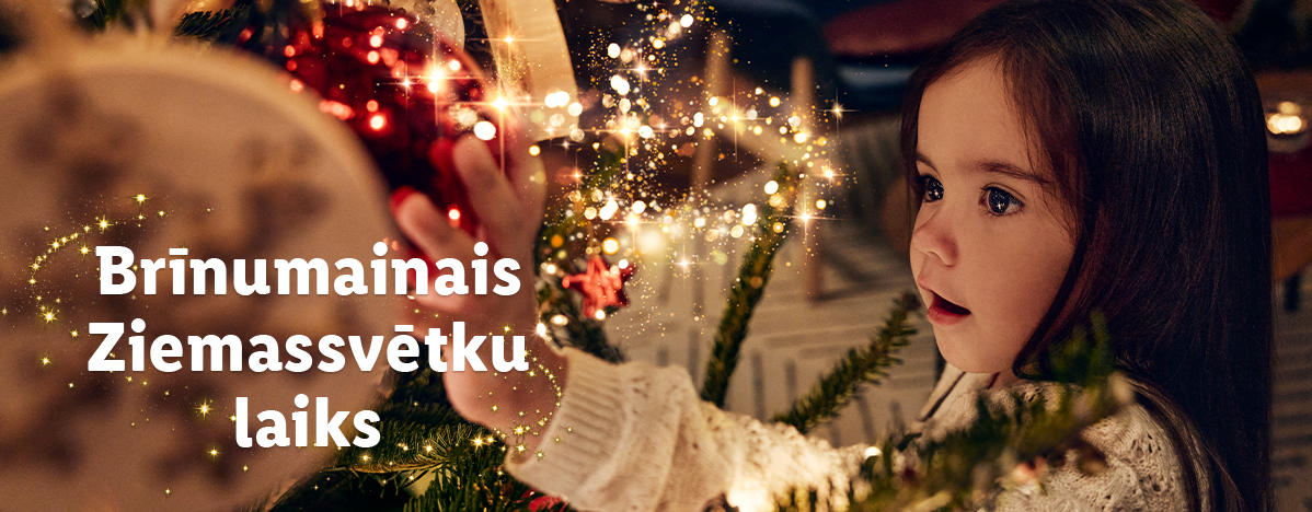 Meitene rotā Ziemassvētku eglīti ar sarkanām un zelta krāsas rotājumiem.