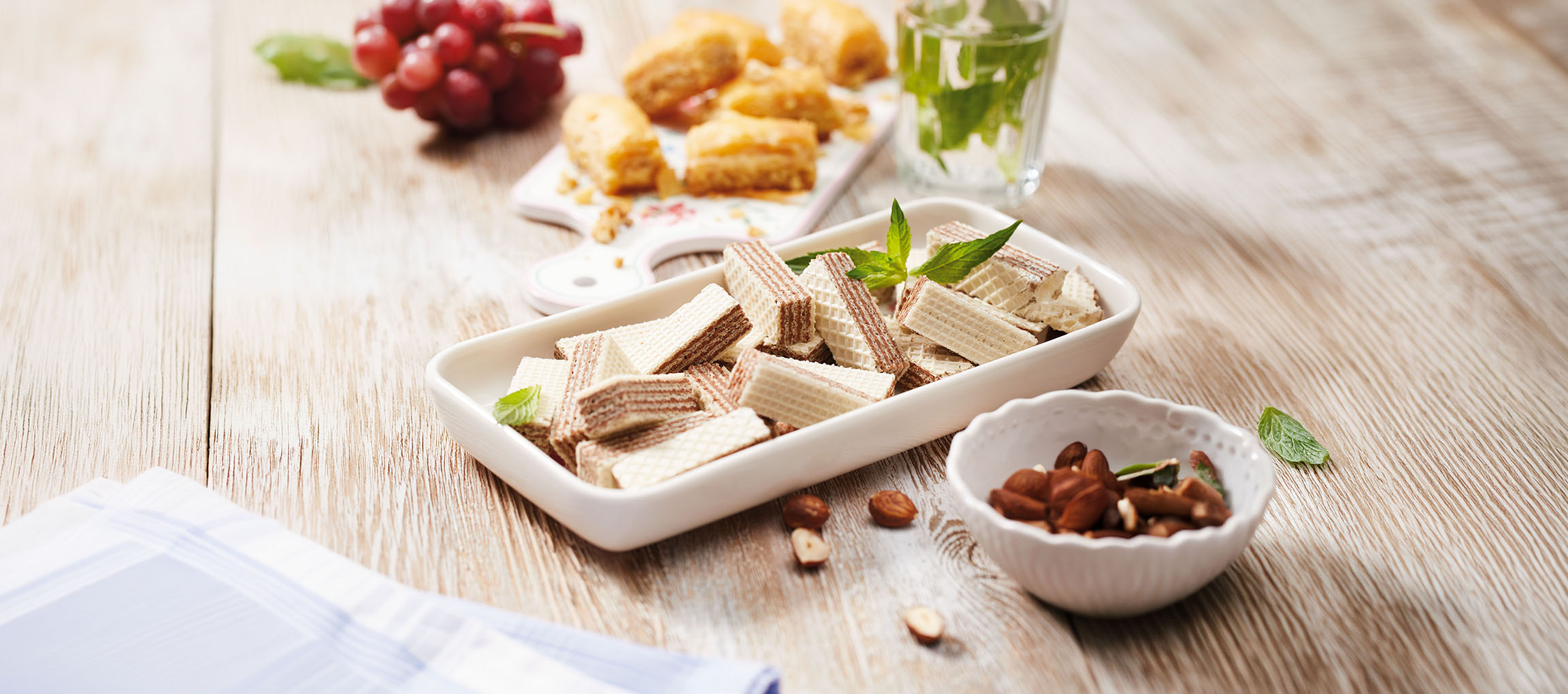 Vafeļu cepumi, baklava, vīnogas un piparmētru ūdens uz koka galda.
