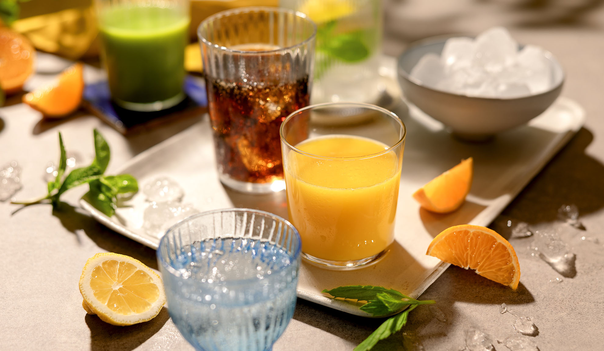 Dažādi atsvaidzinoši dzērieni ar ledu, citrusaugļu šķēlītēm un piparmētrām uz paplātes.