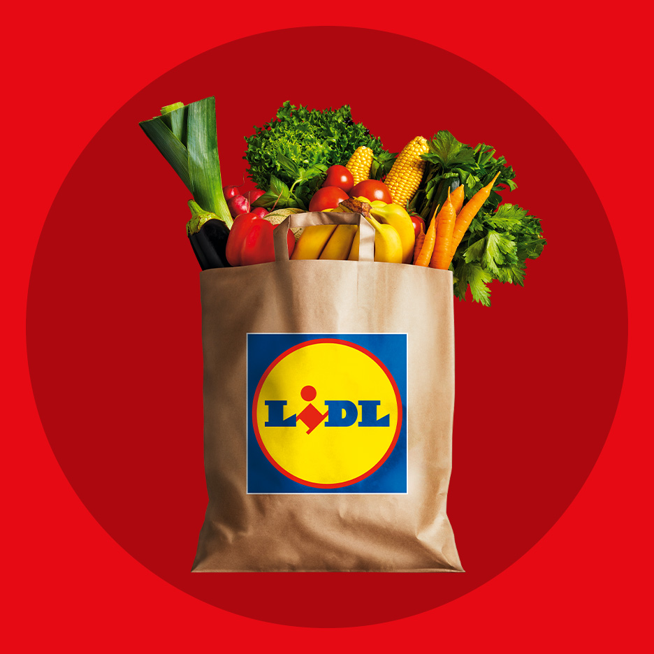 Lidl papīra maisiņš, pilns ar svaigiem augļiem un dārzeņiem uz sarkana fona.