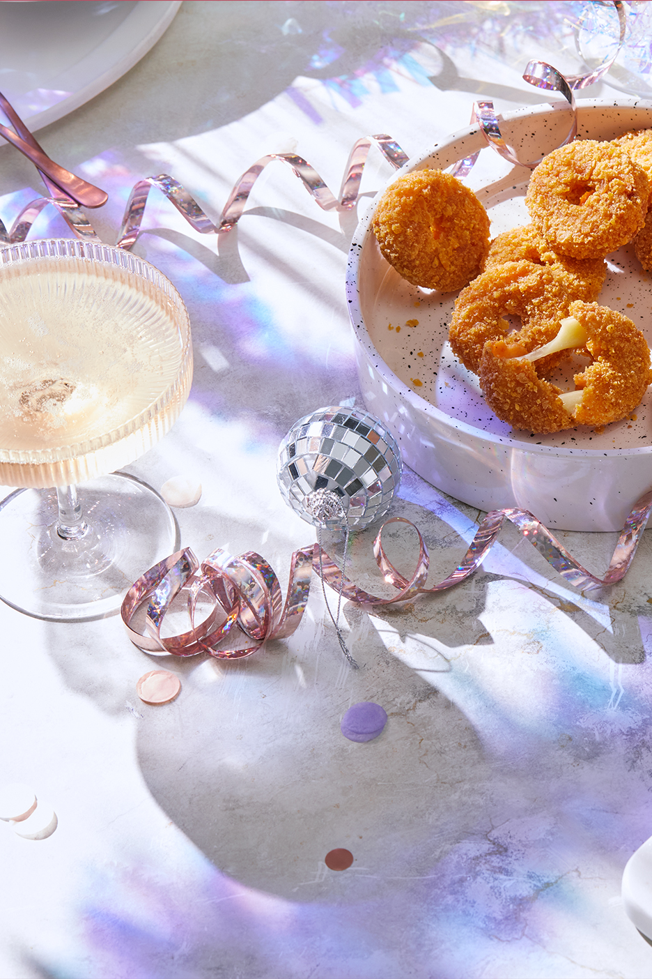 Svētku galds ar šampanieti, ceptu sieru un konfeti.