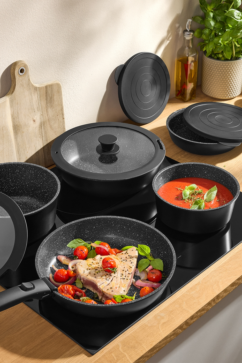 Melnu virtuves trauku komplekts ar nepiedegošu pārklājumu uz indukcijas plīts ar ēdienu.