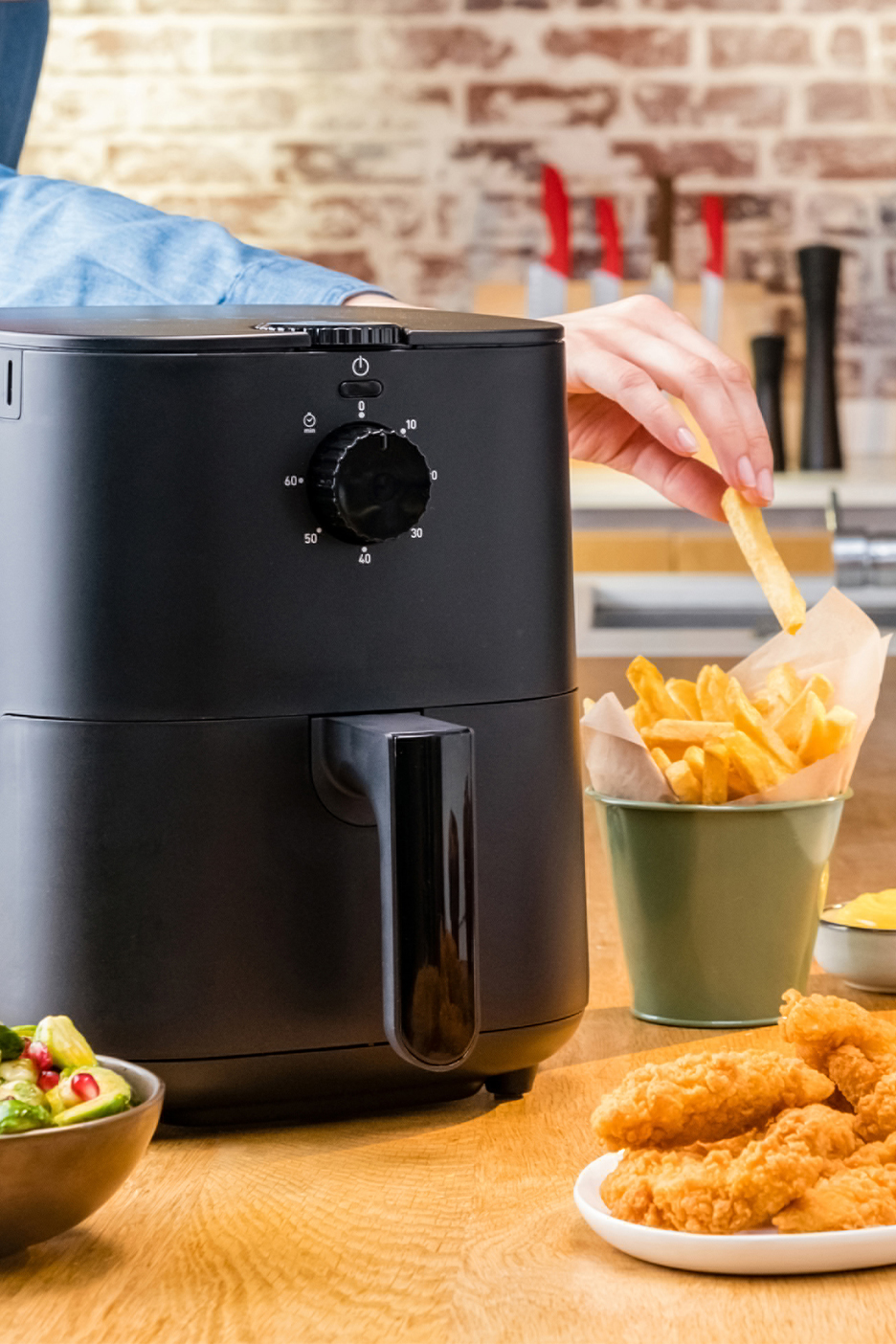 Melna gaisa friteris ar frī kartupeļiem, vistas nagetiem un salātiem uz koka galda.