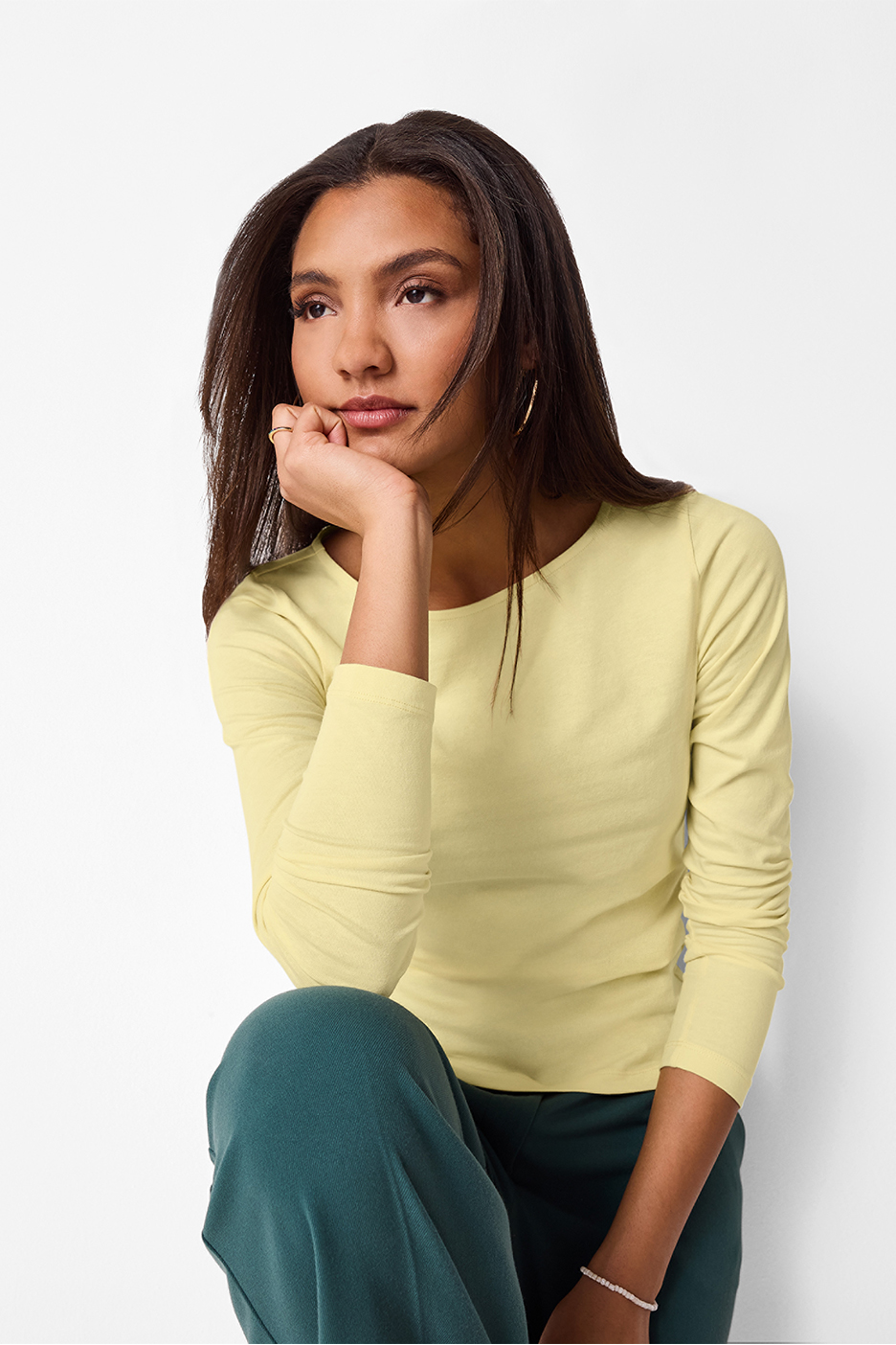 Sieviete dzeltenā blūzē ar garām piedurknēm un tumši zaļās biksēs