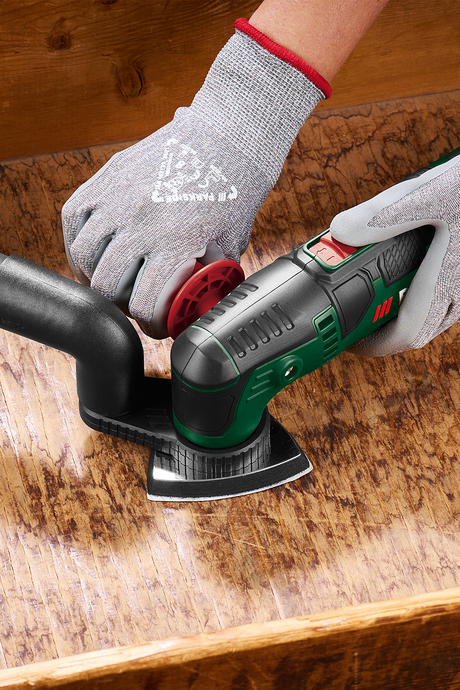 Cilvēks cimdos slīpē koka virsmu ar Parkside daudzfunkcionālo instrumentu.