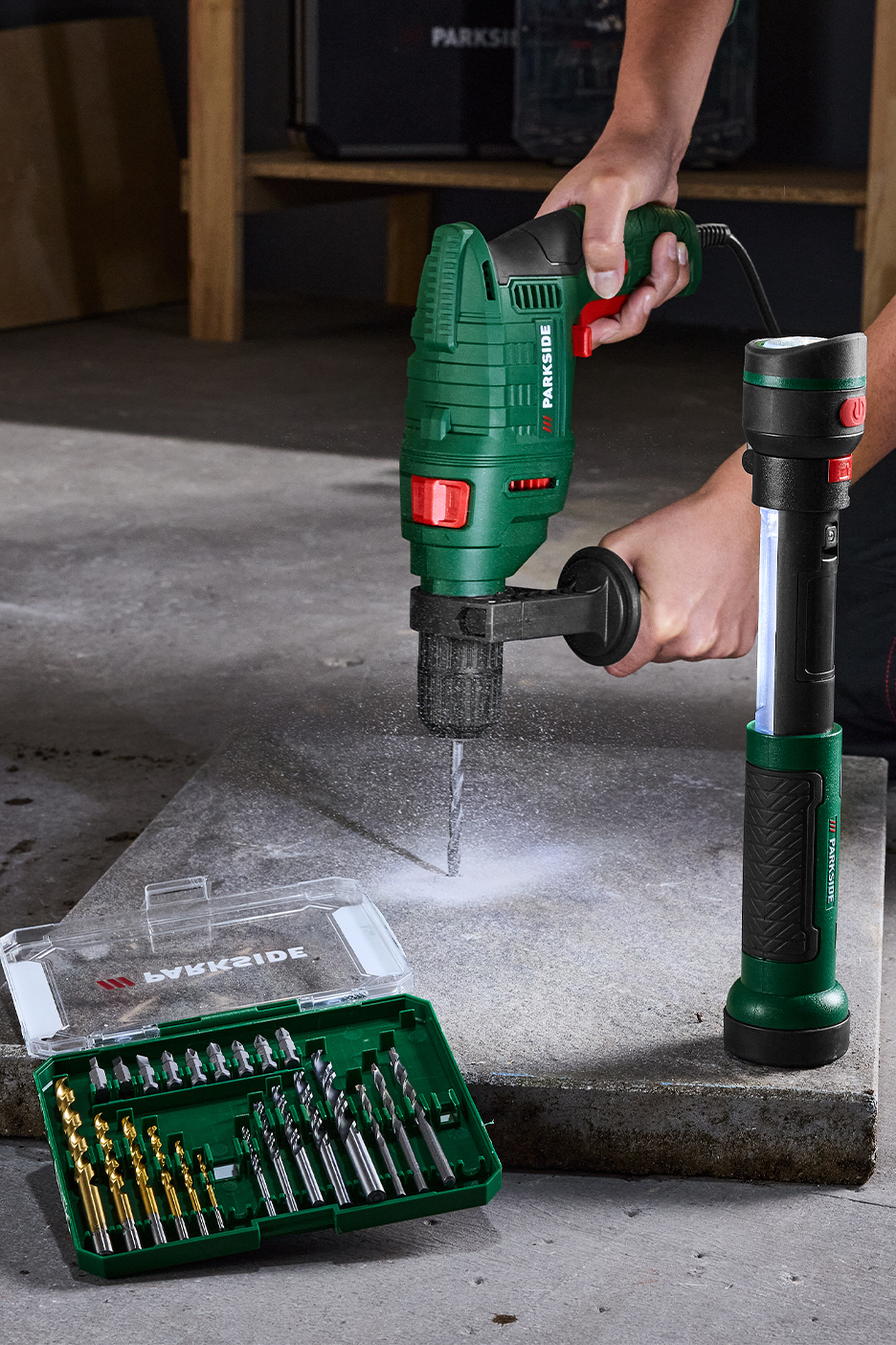 Parkside urbjmašīna urbj betonu, blakus Parkside lukturis un urbju komplekts.