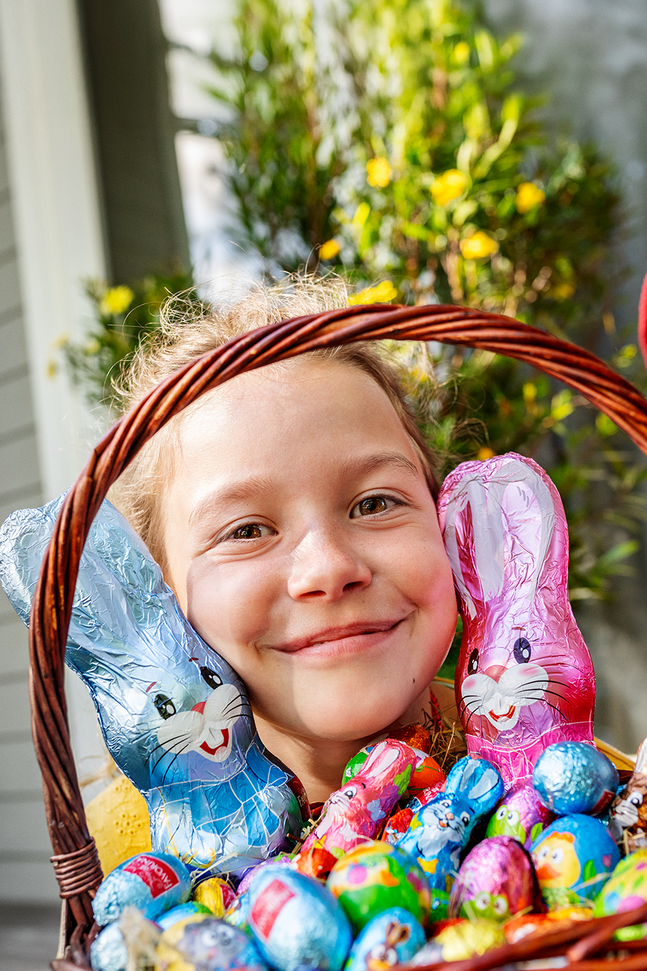 Smaidīgs bērns ar grozu, pilnu ar šokolādes Lieldienu zaķiem un olām.