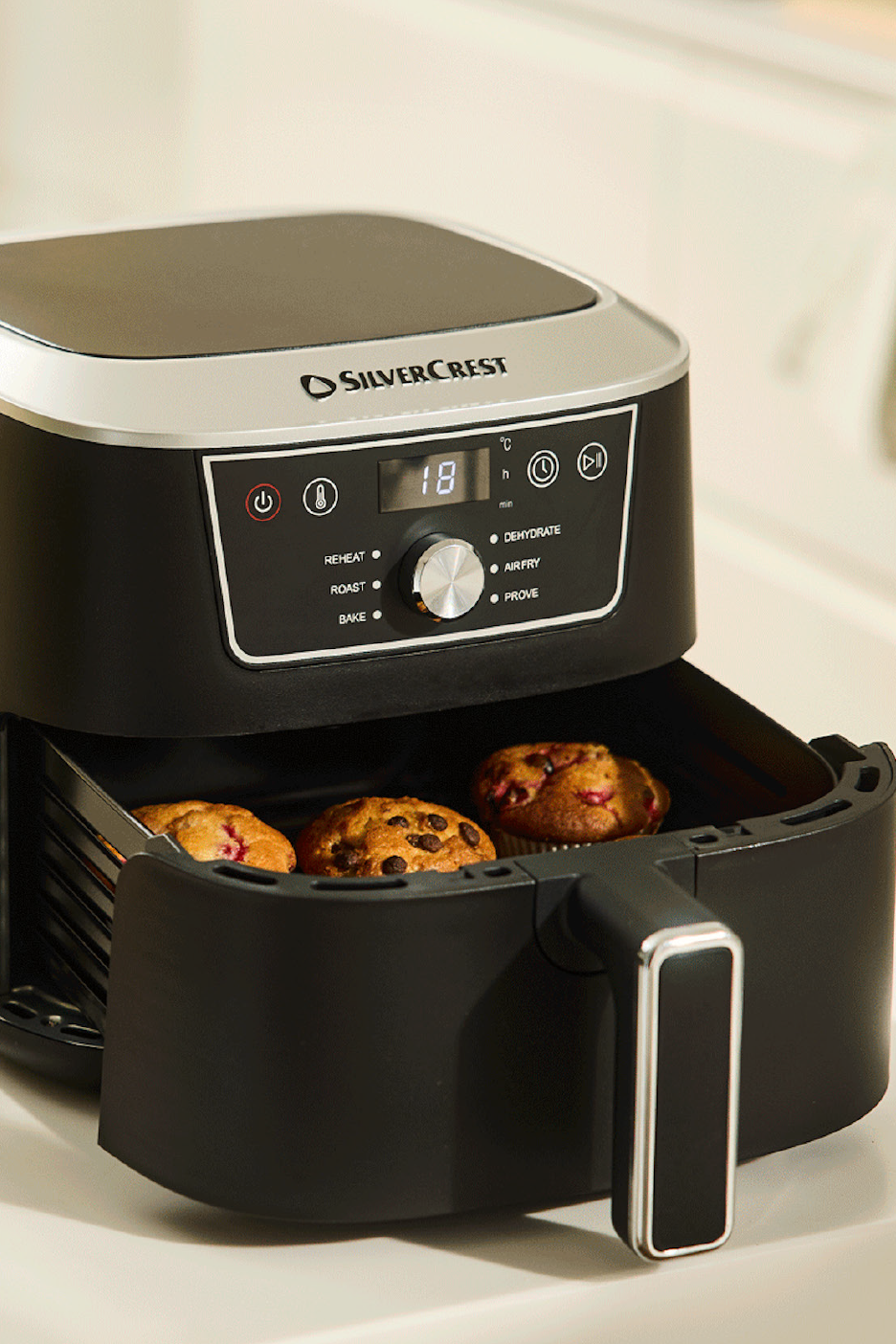 Melna gaisa friteris ar kēksiņiem, digitālo displeju un vadības pogām.