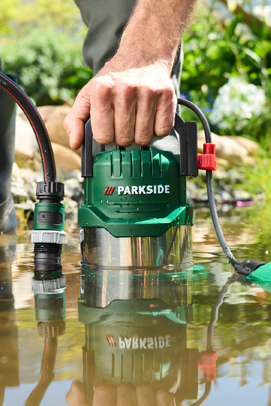 Vīrietis iegremdē zaļu sūkni ūdenī, blakus šļūtene.