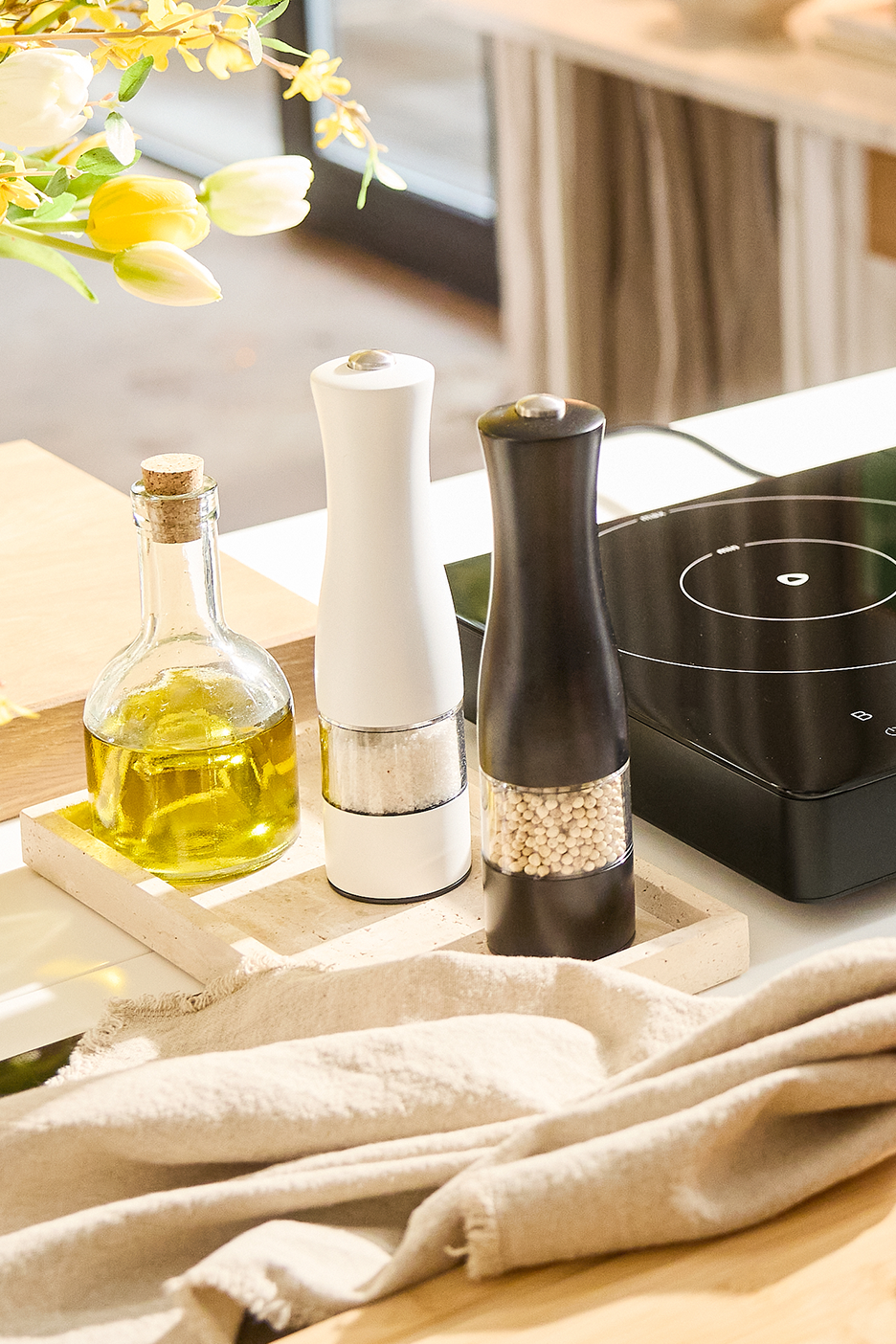 Eļļas pudele, balta un melna sāls un piparu dzirnaviņas uz paplātes