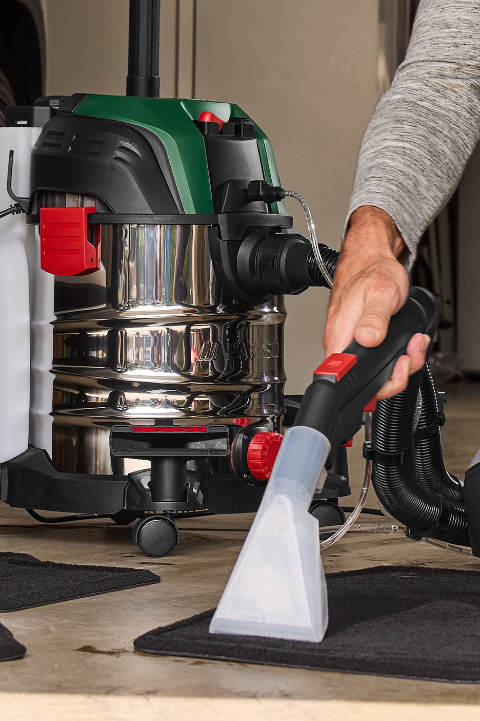 Мужчина чистит автомобильный коврик моющим пылесосом Parkside.