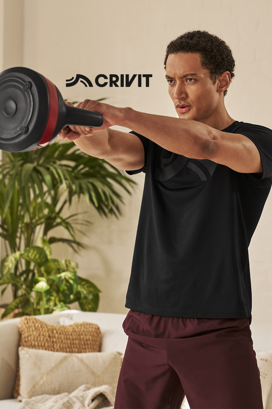 Vīrietis melnā T-kreklā un bordo šortos trenējas ar Crivit trenažieri.