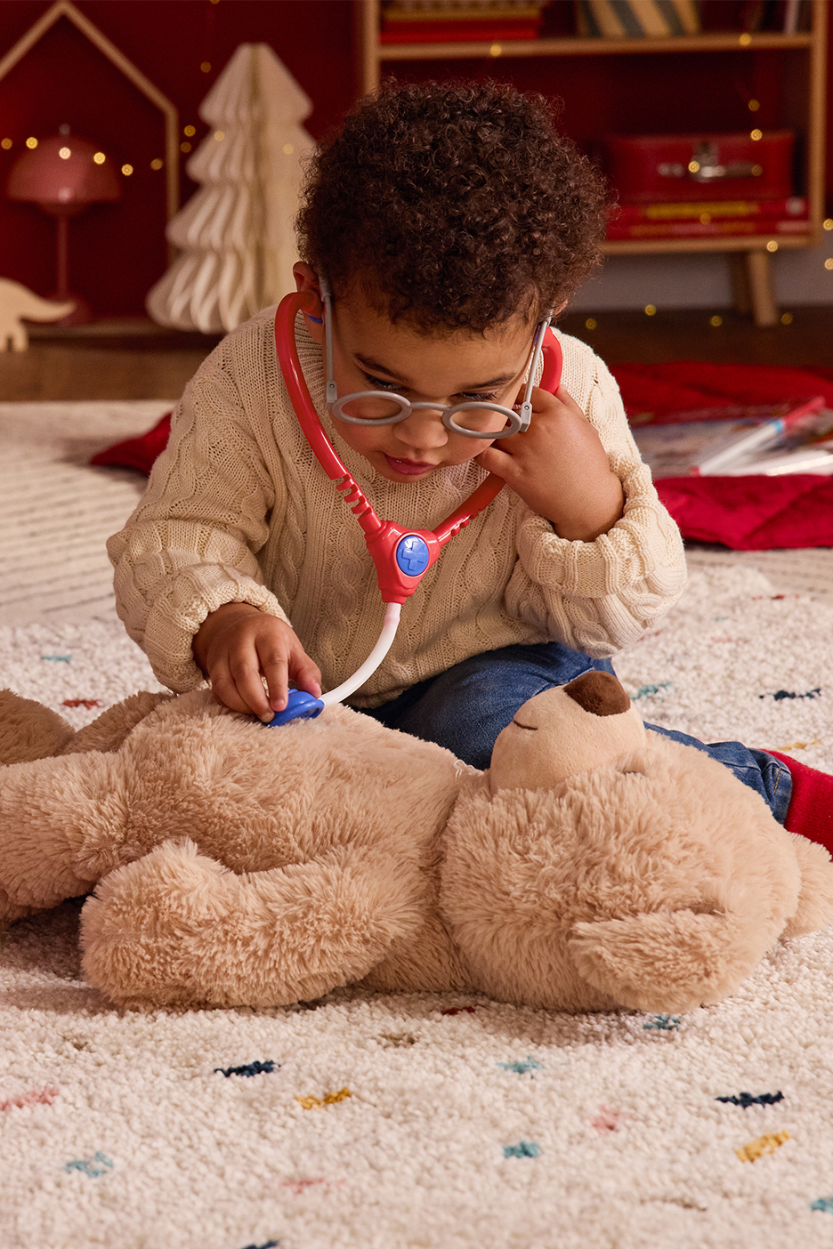 Mazulis spēlējas ar rotaļu stetoskopu un lācīti uz pūkaina paklāja.