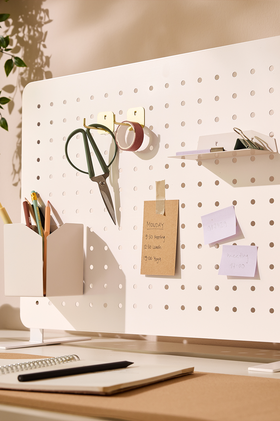 Balta perforēta dēlis ar šķērēm, zīmuļiem, piezīmēm un plauktu kancelejas piederumiem.