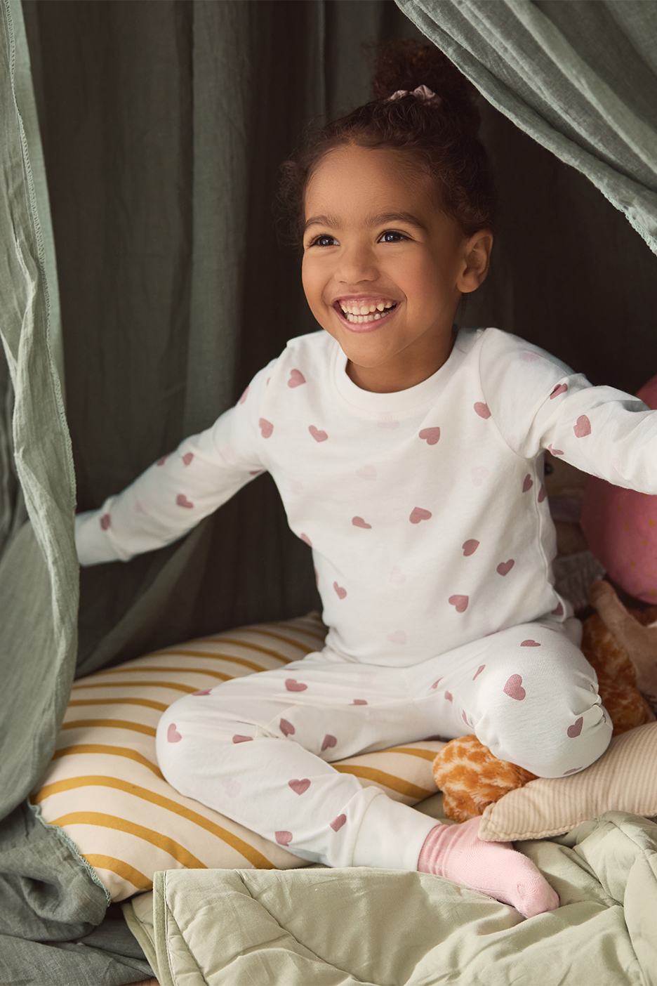 Meitene baltā pidžamā ar sirsniņām sēž mājīgā stūrītī.