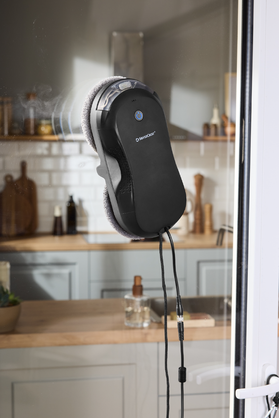 Logu tīrītājs tīra stiklu, atspoguļojot virtuves interjeru.