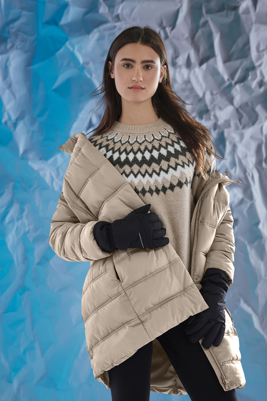 Sieviete bēšā stepētā jakā, džemperī ar rakstu un melnos cimdos