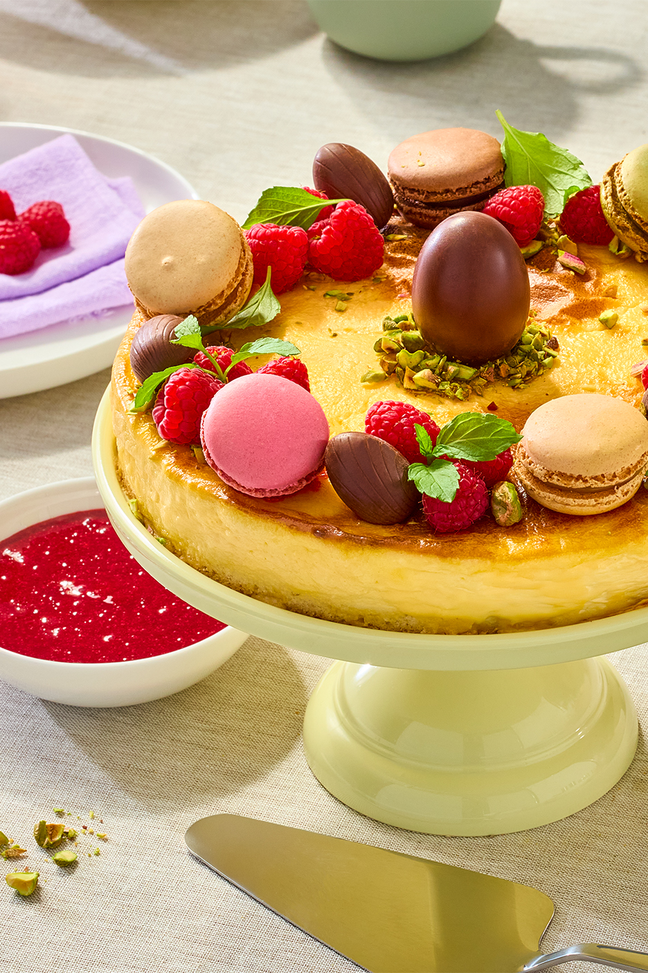 Siera kūka ar avenēm, makaroniem un šokolādes olām uz gaiši zaļa statīva.