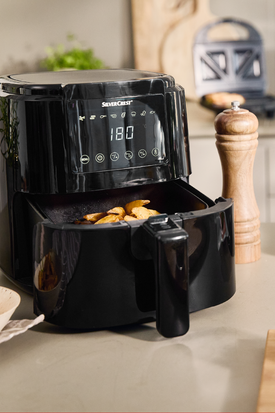 Melna gaisa friteris ar kartupeļu daiviņām, kas gatavojas, un digitālo displeju, kas rāda 180.