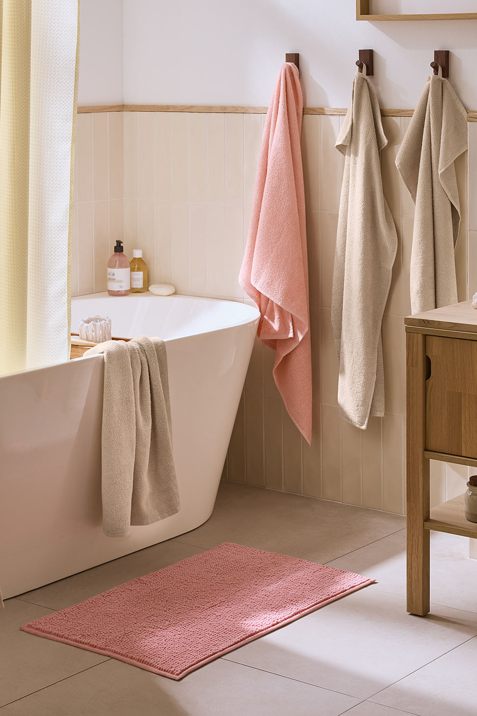 Vannas istaba ar rozā paklājiņu, dvieļiem un baltu vannu.