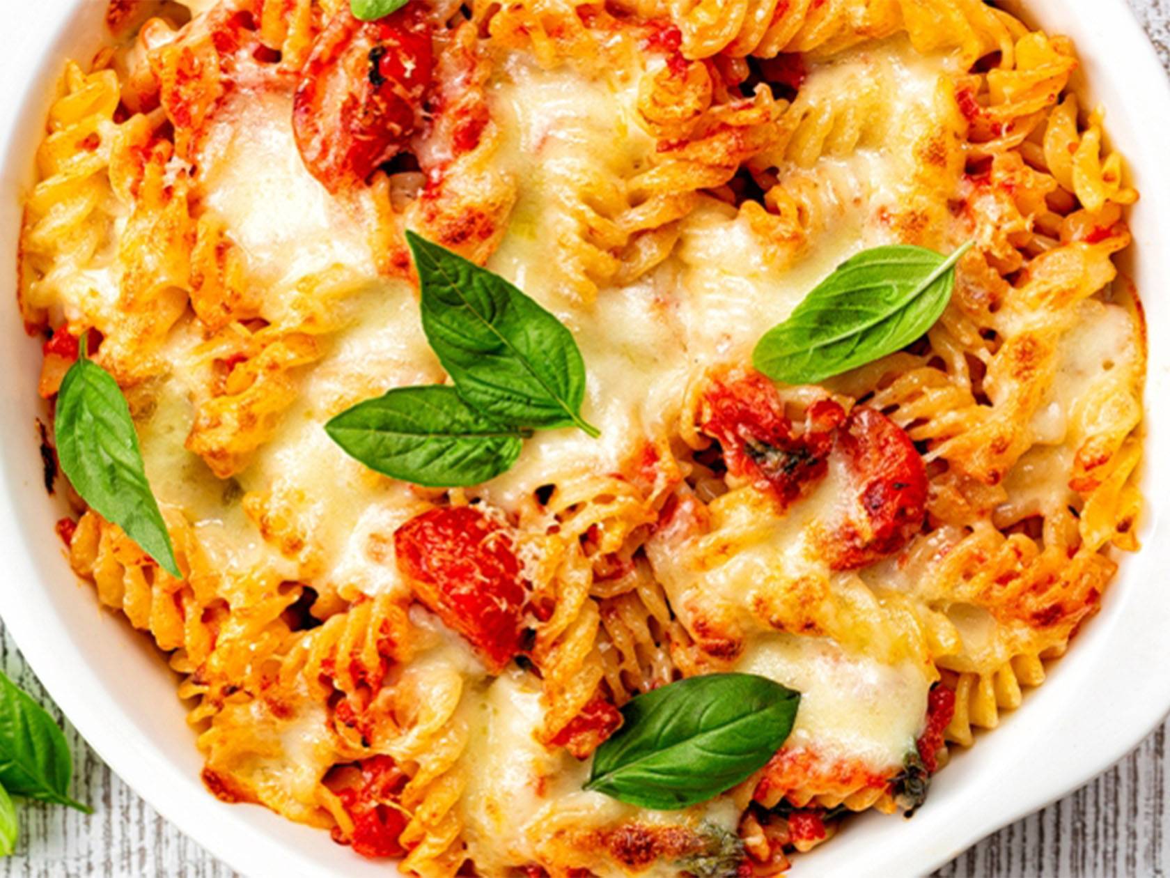 Cepta pasta ar tomātiem un mocarellu, dekorēta ar baziliku.