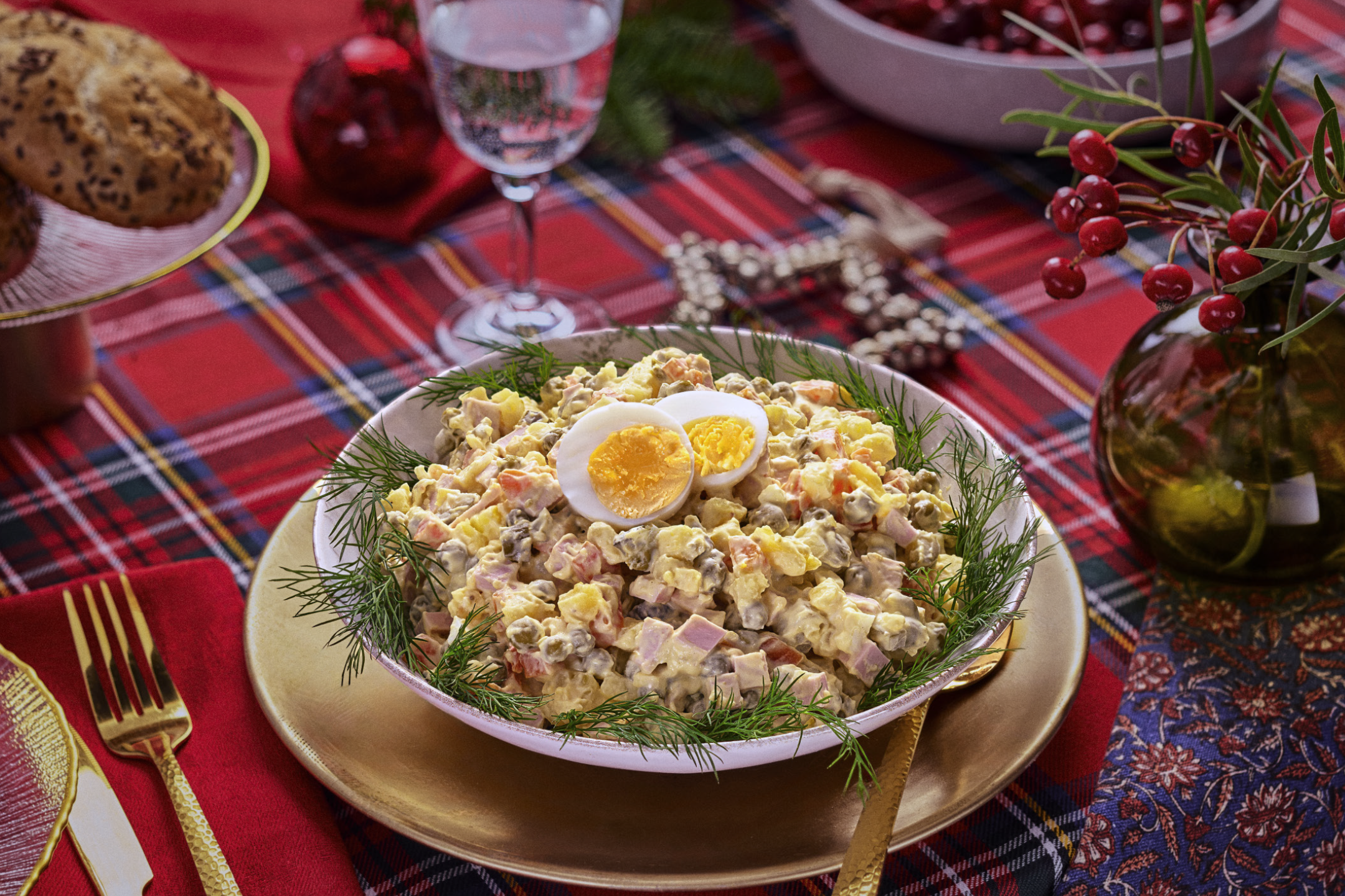 Olivier salāti ar olām un dillēm uz svētku galda ar rūtainu galdautu.