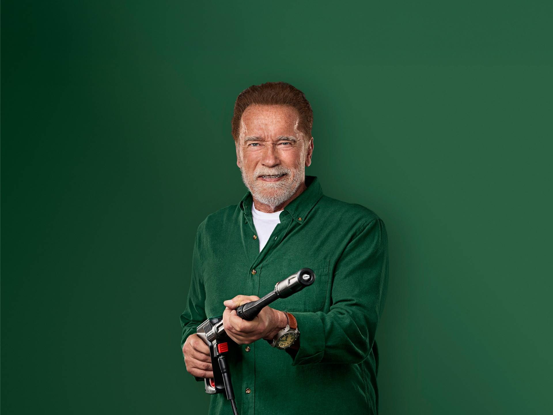 Arnolds Švarcenegers smaida, turot augstspiediena mazgāšanas pistoli.