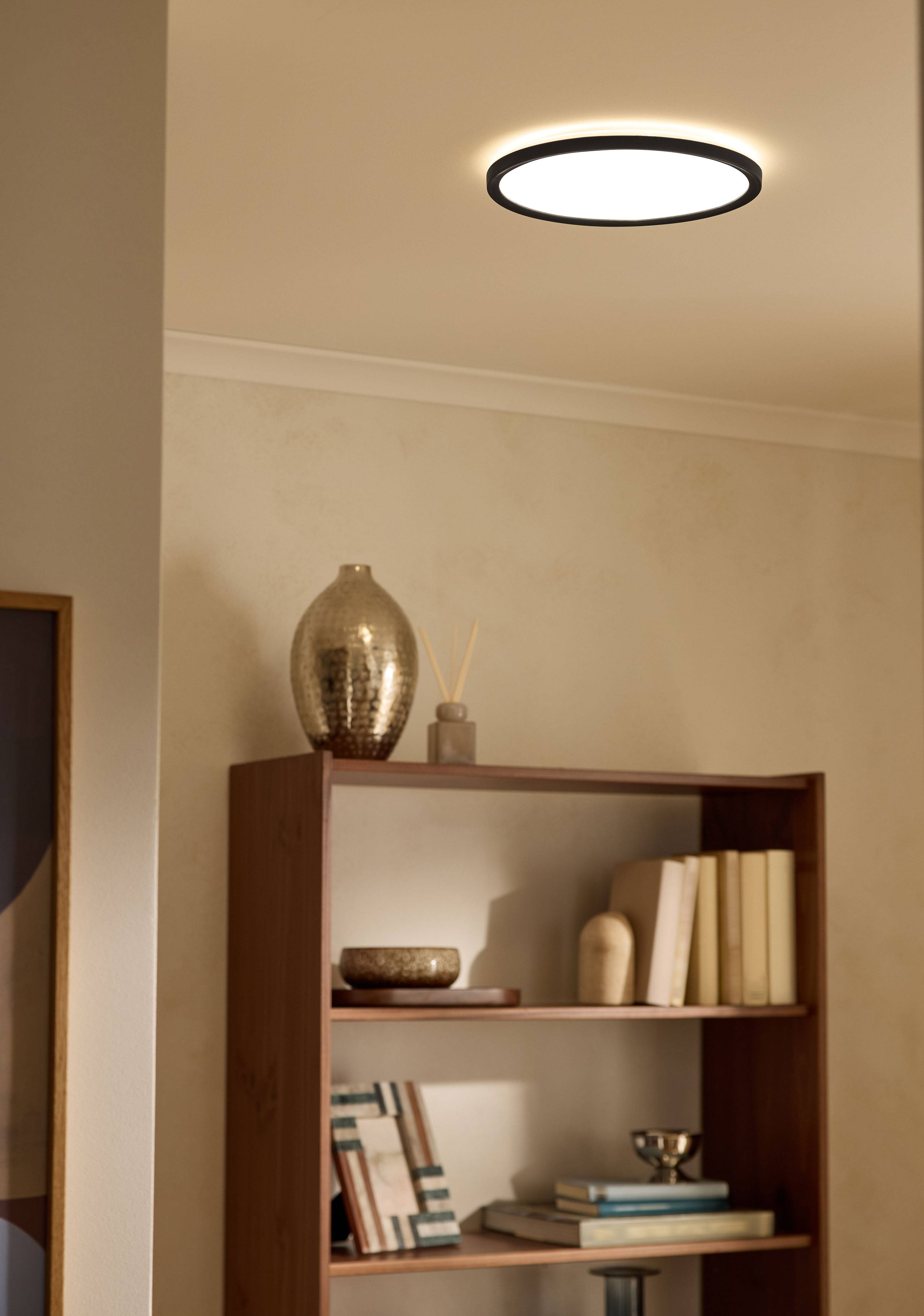 Griestu lampa apgaismo viesistabas grāmatu plauktu ar grāmatām un dekoriem.