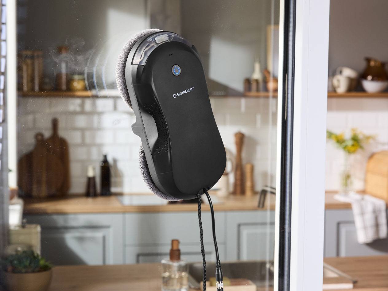 Робот-мойщик окон Silvercrest на оконном стекле с кухней на заднем плане.