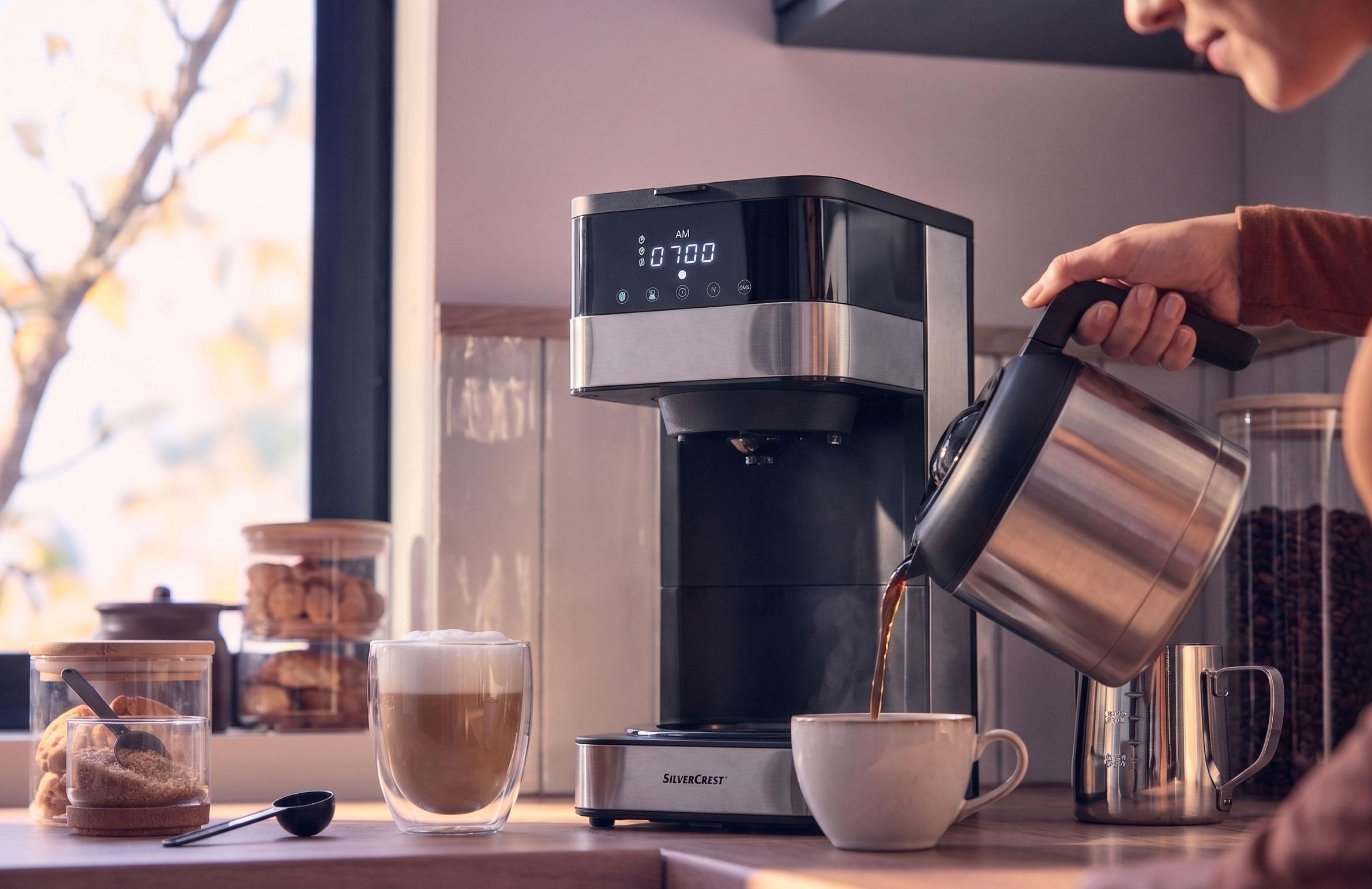 Kafijas automāts lej kafiju krūzē, ar latte un cepumiem uz letes.