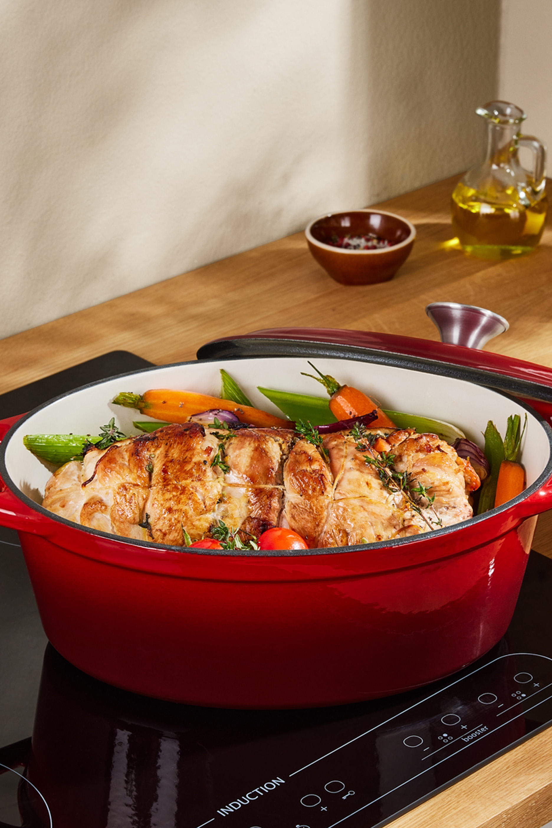 Sarkans čuguna katls ar ceptu gaļu un dārzeņiem uz indukcijas plīts.