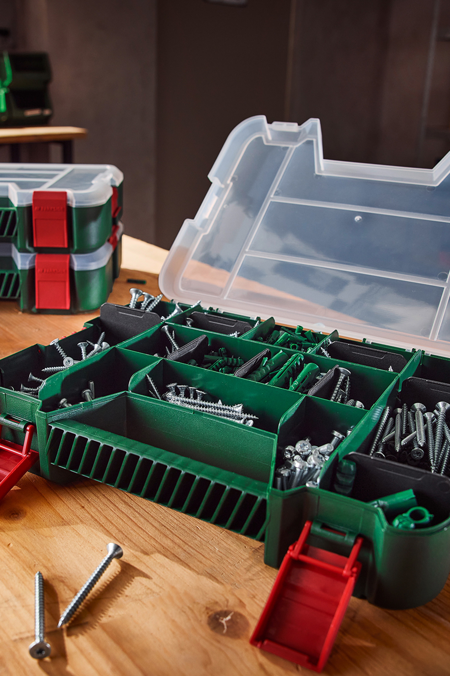 Atvērta zaļa instrumentu kaste ar skrūvēm un dībeļiem uz koka galda.