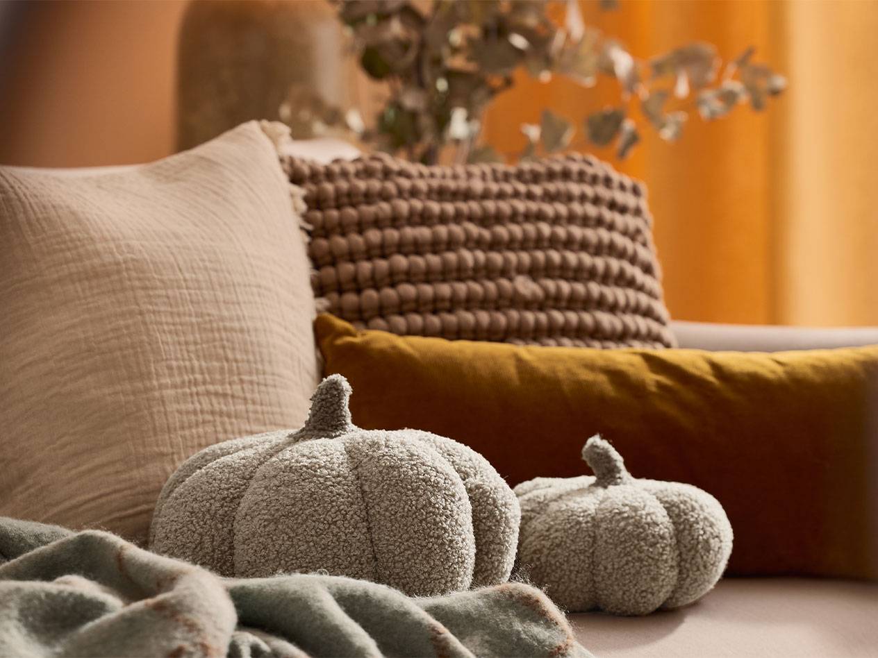 Две плюшевые декоративные тыквы и подушки в земляных тонах на диване.
