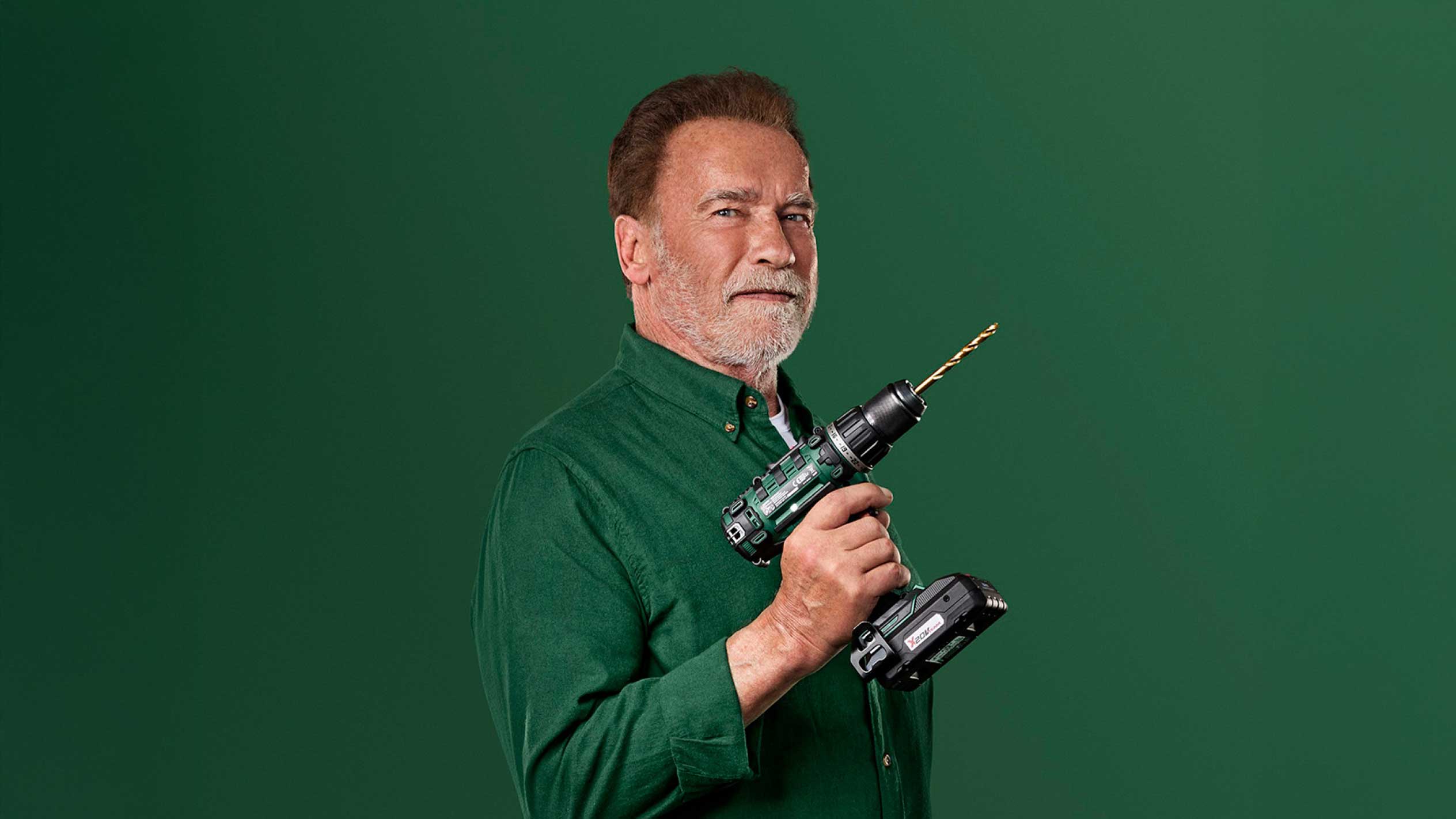 Arnolds Švarcenegers tur zaļu bezvadu urbi ar zelta urbi.