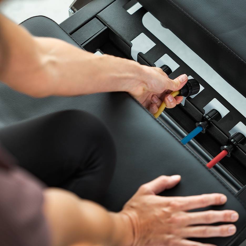 Человек регулирует эспандеры на скамье для упражнений.