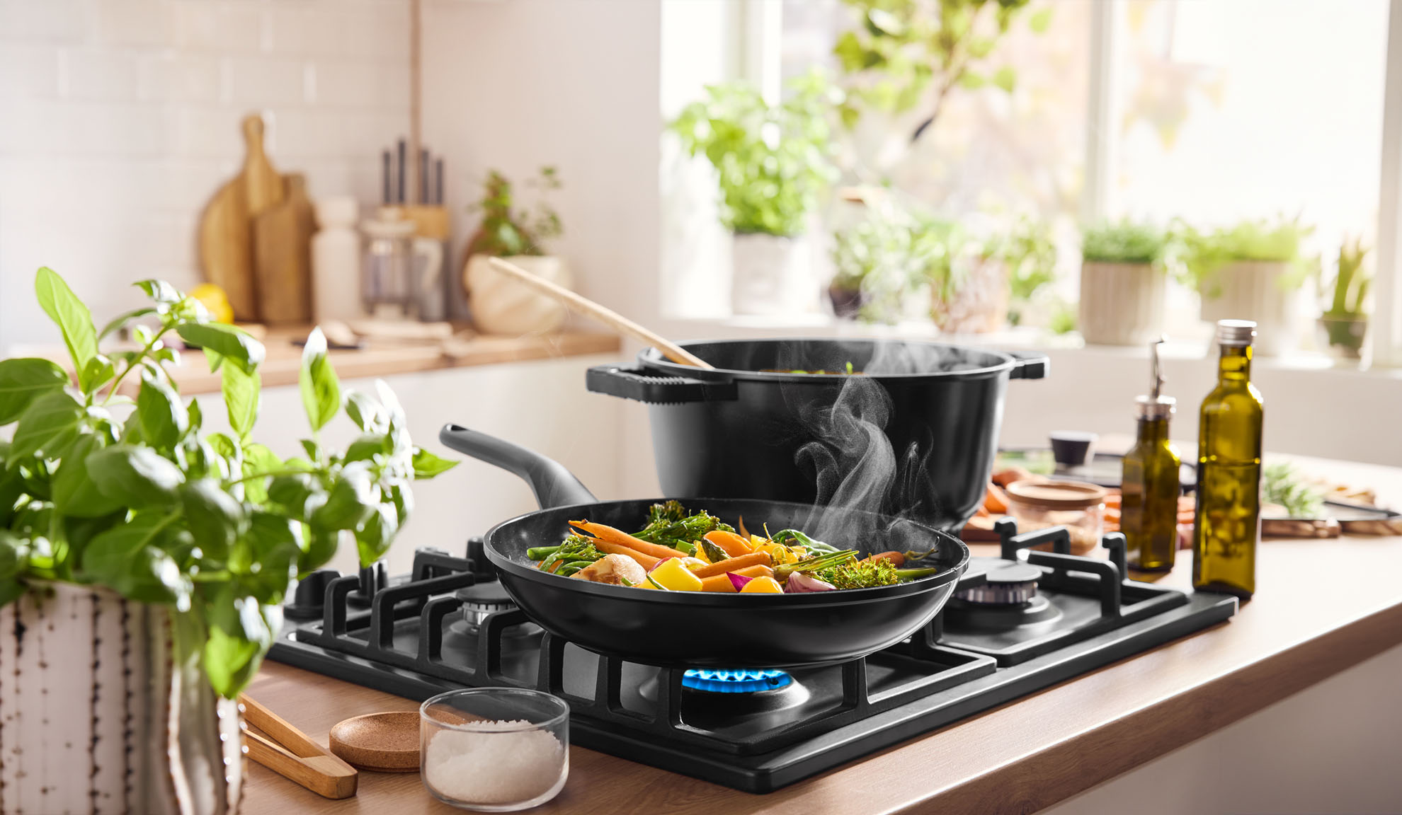 Готовящиеся на пару овощи в сковороде и кастрюле на газовой плите на светлой кухне.