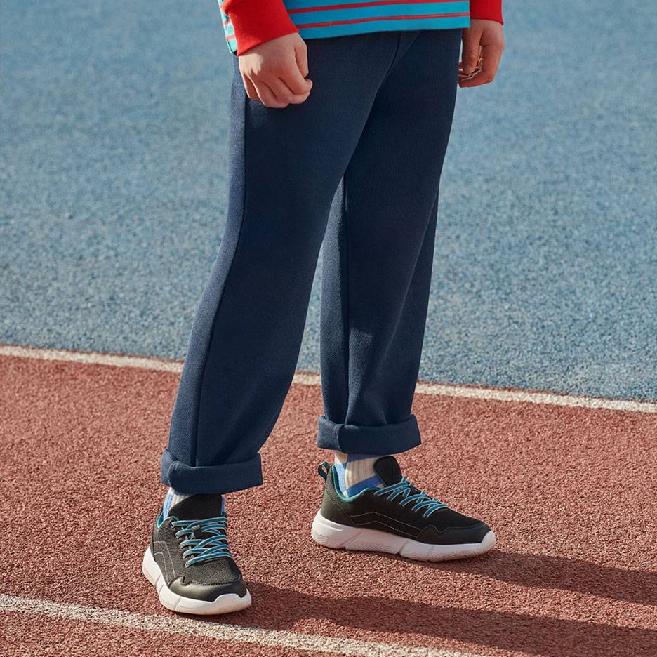 Tumši zilas sporta bikses un melni sporta apavi ar zilām auklām uz skrejceļa.