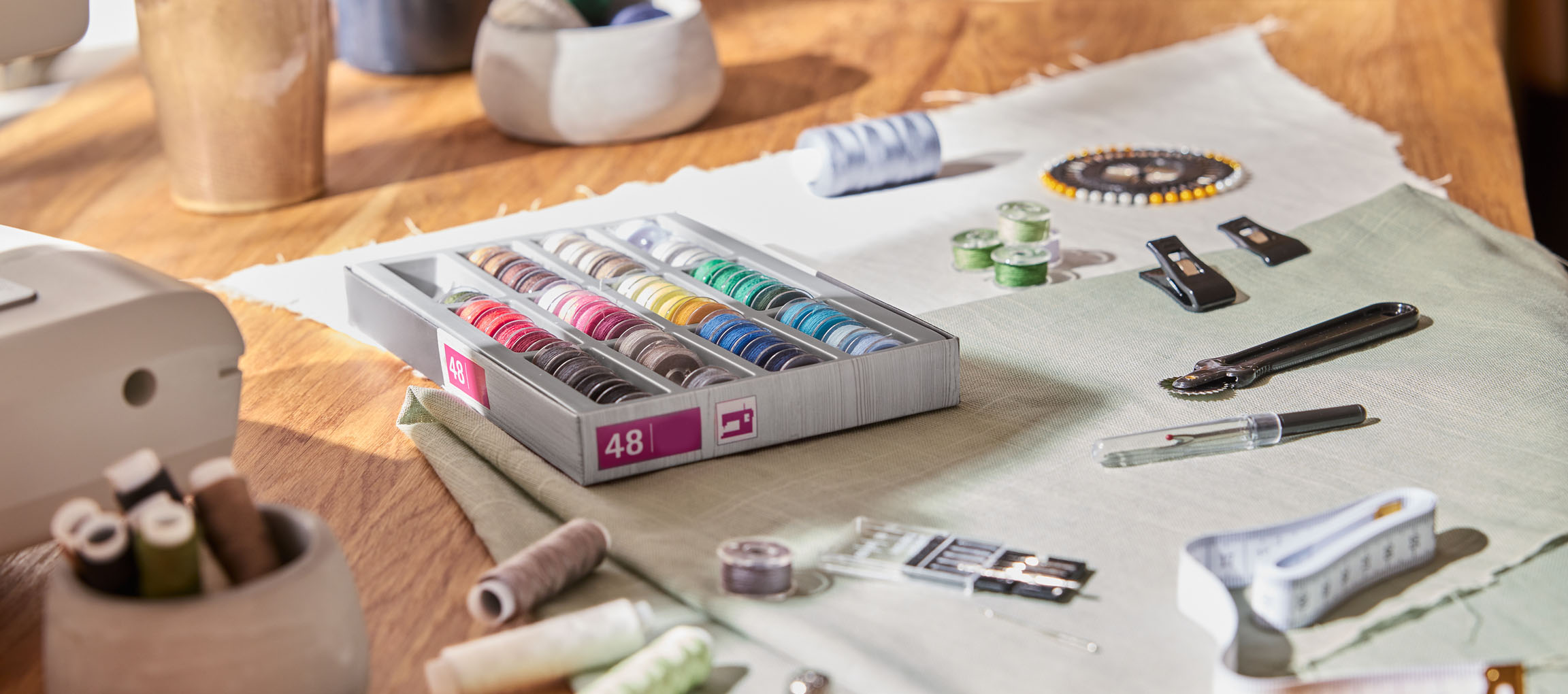 Šūšanas piederumi uz koka galda, tostarp diegu organizators ar 48 spolēm, audums un dažādi instrumenti.