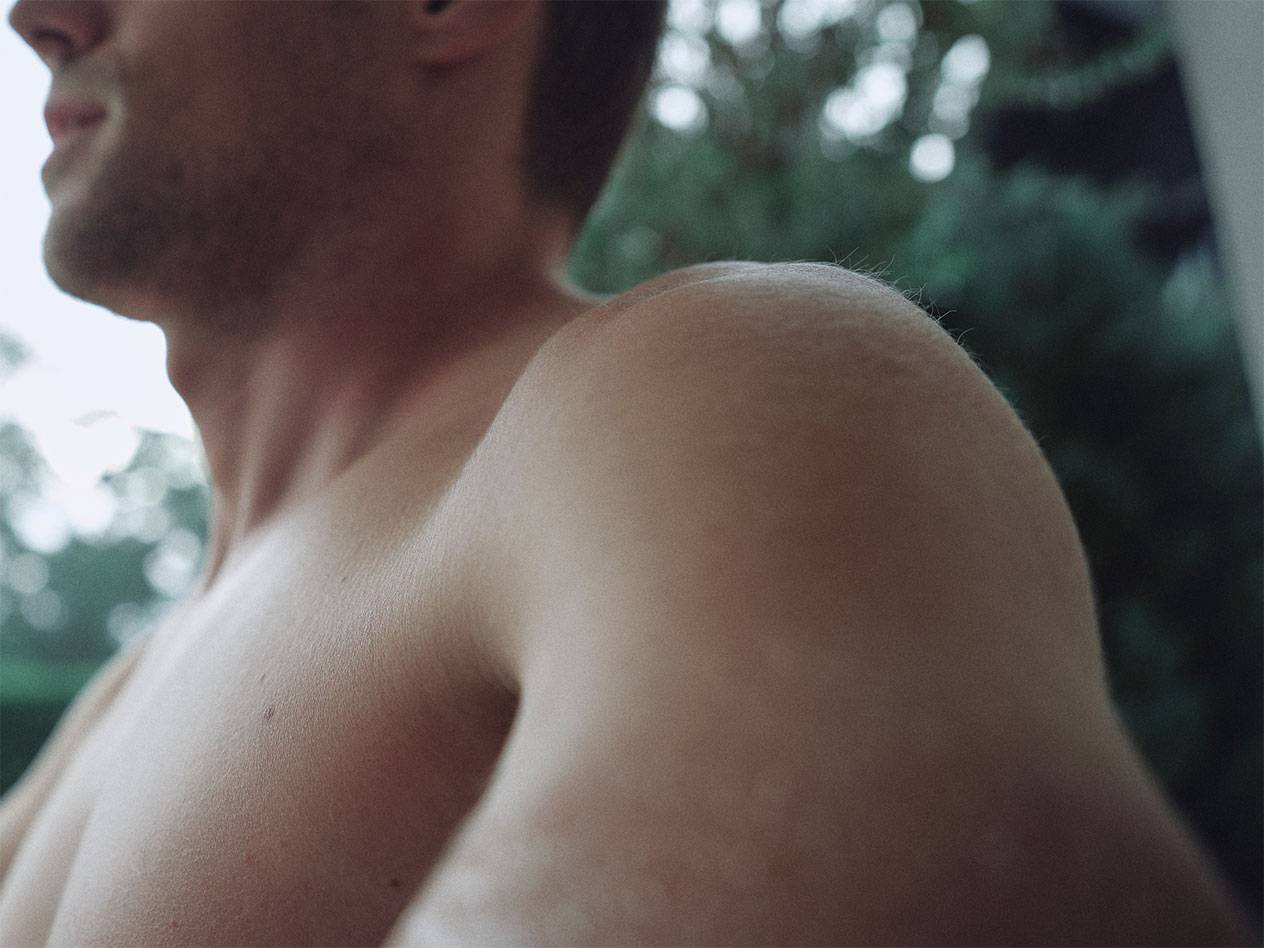 Крупный план плеча и шеи мужчины на размытом зеленом фоне.