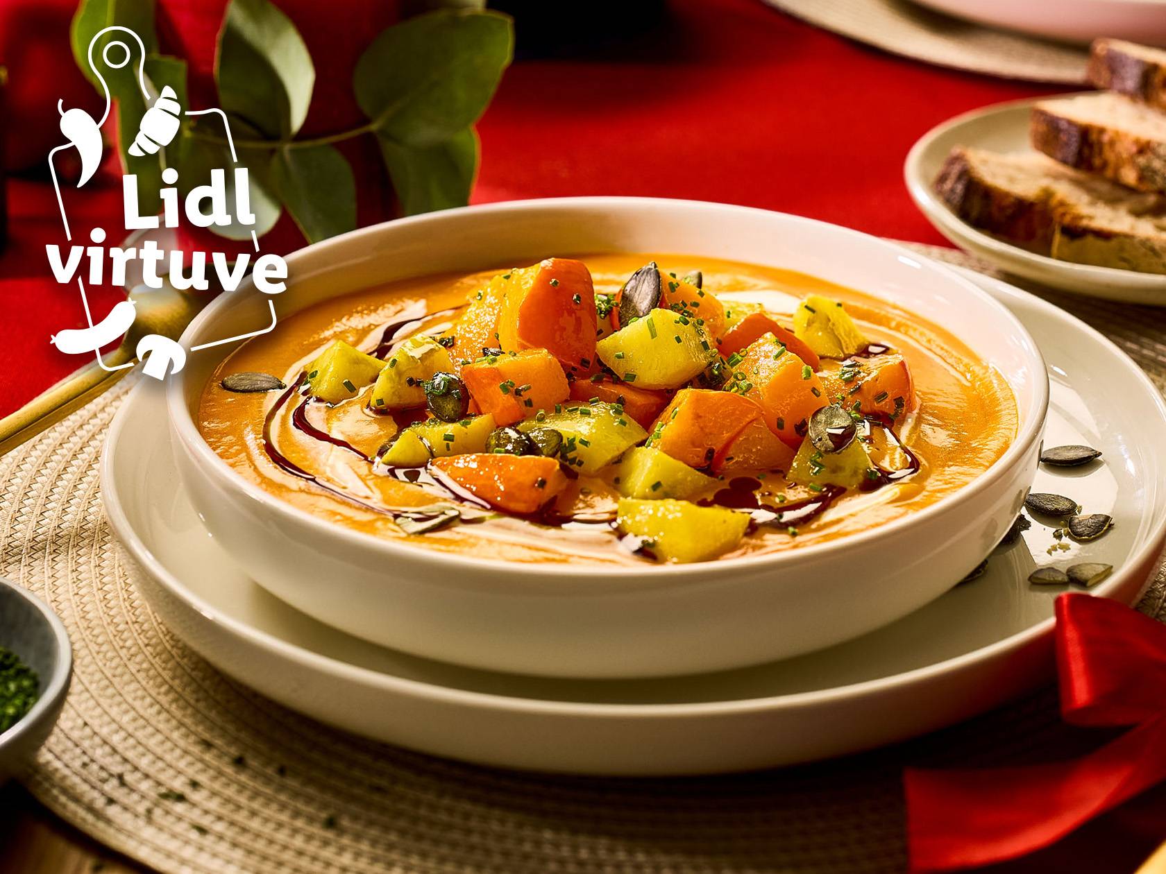 Lidl virtuve: Krēmzupa ar ķirbi, kartupeļiem un sēklām uz sarkana galda.