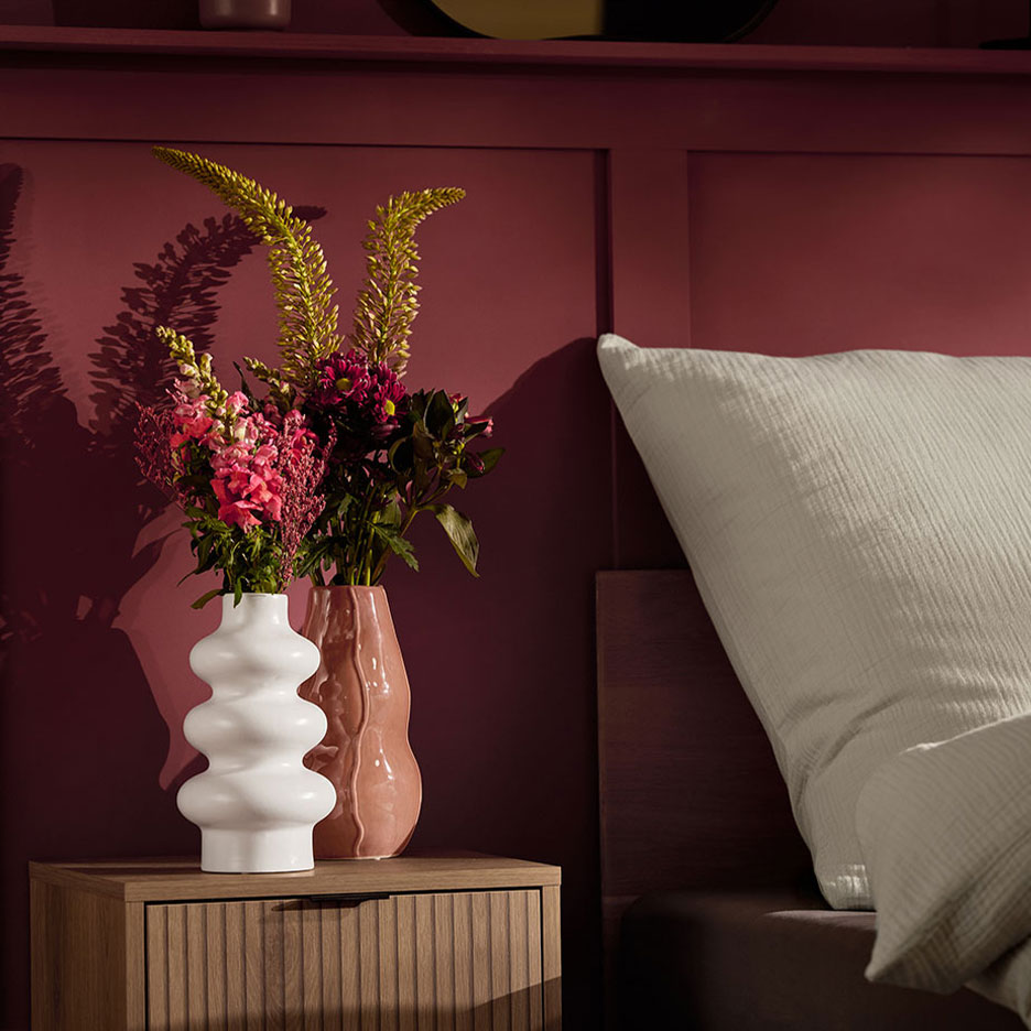 Две вазы с цветами на тумбочке рядом с кроватью с белой подушкой.