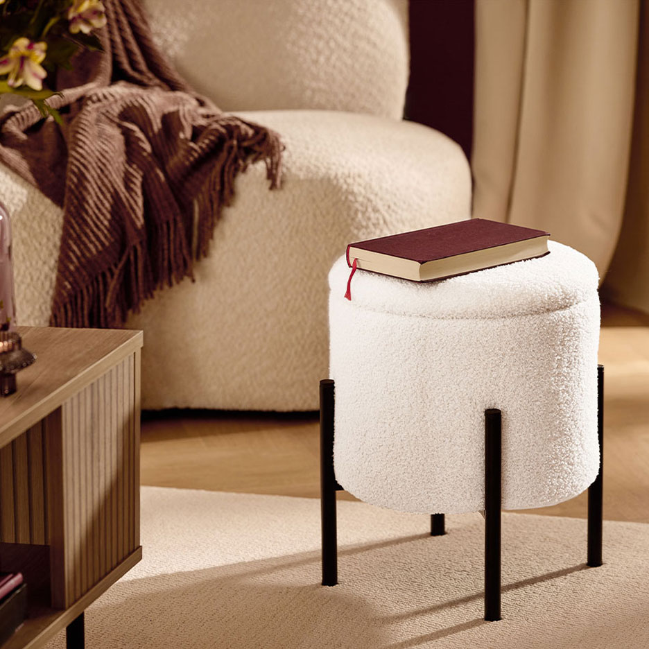 Белый пушистый табурет с черными ножками, красная книга, кресло и коричневый плед.