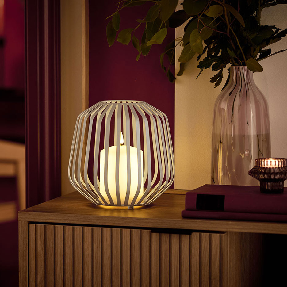 Светодиодная свеча в белом металлическом подсвечнике на деревянном комоде.