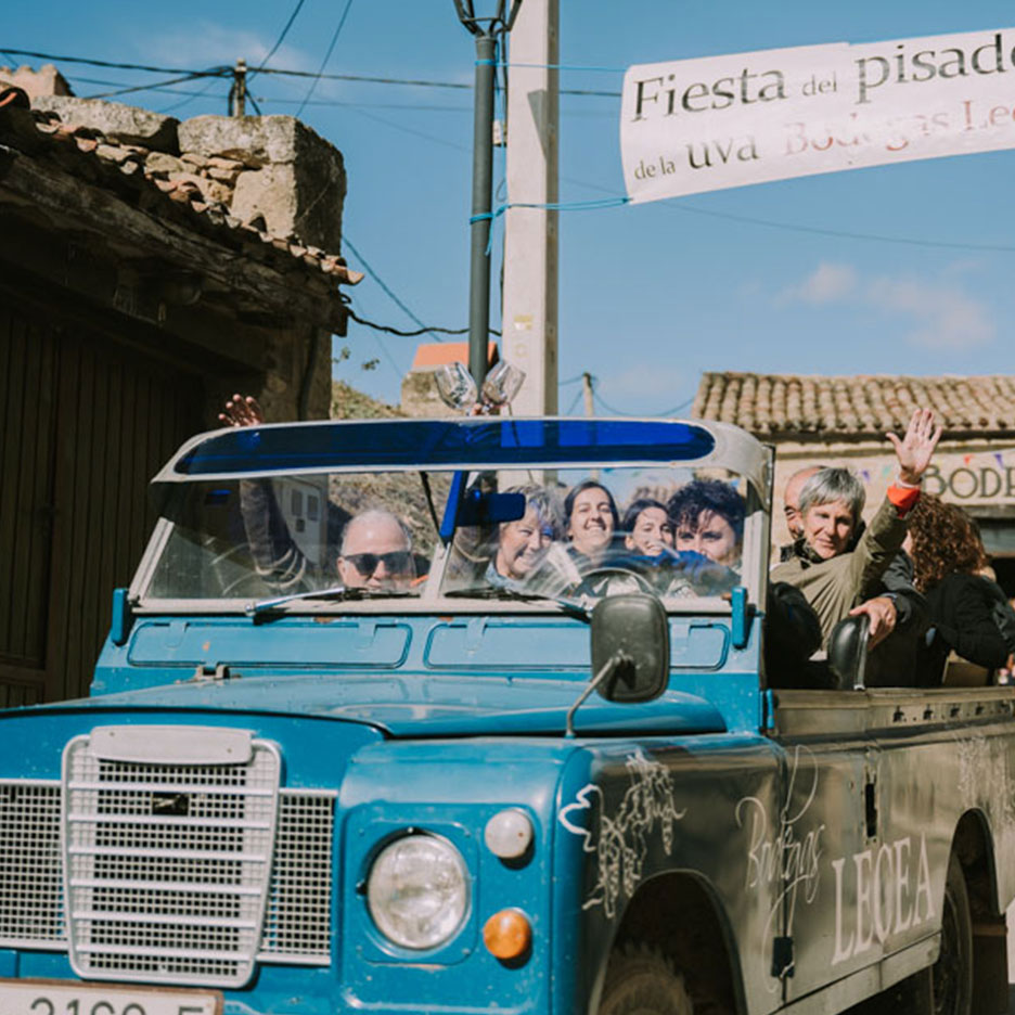 Cilvēki vicina no zila apvidus auto vīna festivāla laikā, ar baneri „Fiesta del pisado de la uva“.
