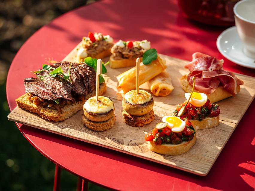 Tapas un uzkodu sortiments, ieskaitot steiku, sēnes, pavasara rullīšus un brusketu.