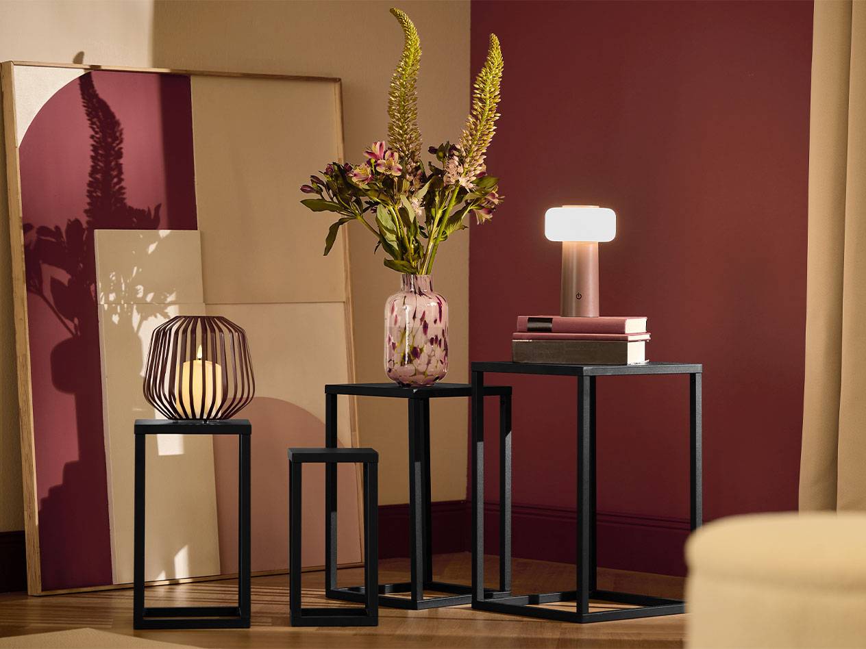 Три черных приставных столика со свечой, вазой цветов и лампой.