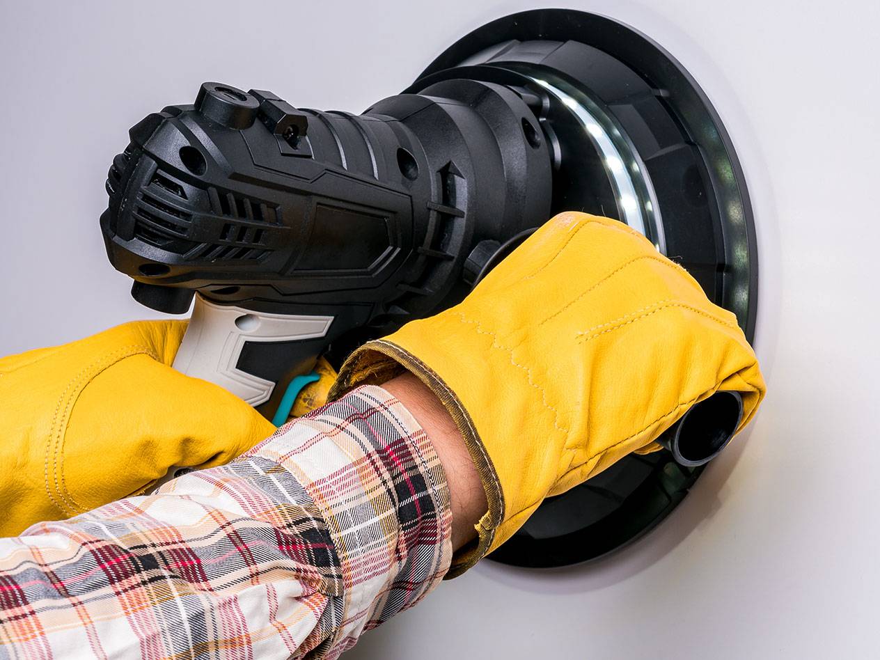 Elektriskā sienu slīpmašīna ar LED gaismu, ko izmanto persona ar cimdiem.