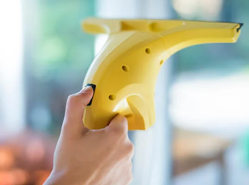 Рука держит желтый электрический стеклоочиститель, моющий окно.